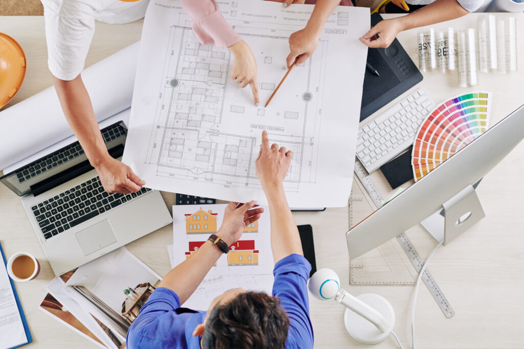 Team of architects and designers pointing at blueprint of commercial building they are working on